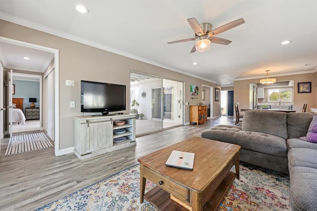 living room with recessed lighting, ceiling fan with notable chandelier, crown molding, and light wood-style floors