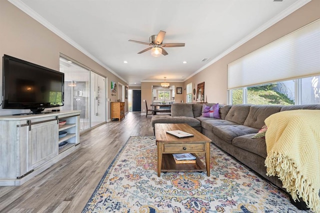 living area featuring a wealth of natural light, light wood-type flooring, ceiling fan, and crown molding