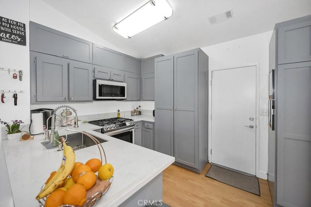 kitchen featuring visible vents, gray cabinets, a sink, white microwave, and stainless steel gas range