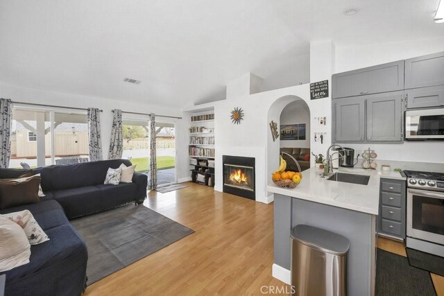 living area with visible vents, built in shelves, lofted ceiling, light wood-style flooring, and a glass covered fireplace