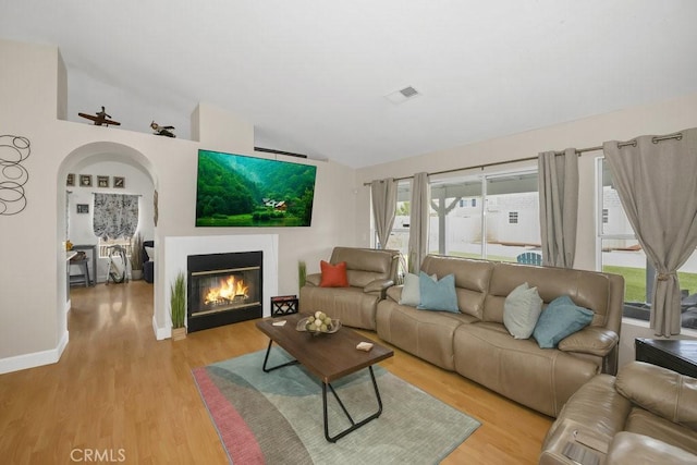 living room with visible vents, a glass covered fireplace, baseboards, light wood finished floors, and lofted ceiling