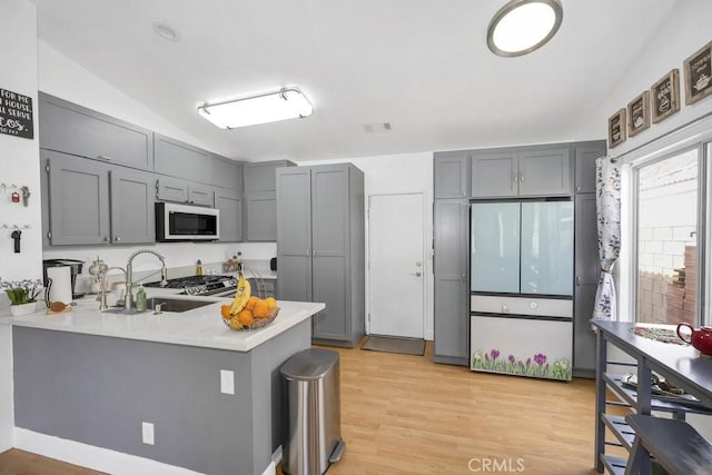 kitchen featuring a sink, a peninsula, white microwave, and gray cabinetry