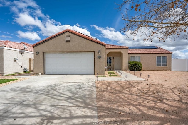 mediterranean / spanish-style home with a tiled roof, concrete driveway, roof mounted solar panels, stucco siding, and a garage