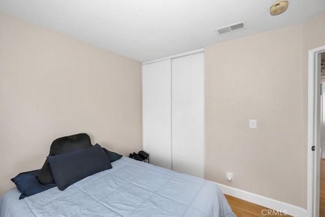 bedroom featuring a closet, visible vents, baseboards, and wood finished floors