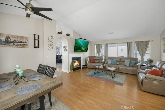 living room with visible vents, light wood-type flooring, a lit fireplace, lofted ceiling, and a ceiling fan