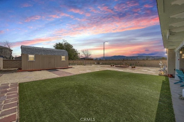 yard at dusk with a patio area, a fenced backyard, a storage unit, and an outdoor structure