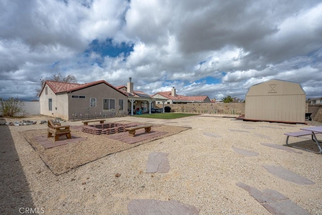 rear view of property featuring a fenced backyard, stucco siding, an outdoor structure, a storage unit, and a tiled roof