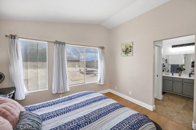 bedroom featuring vaulted ceiling, light wood-style floors, baseboards, and connected bathroom