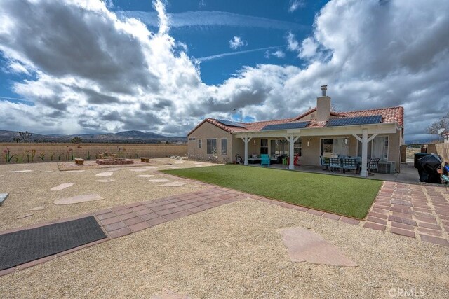 rear view of house featuring a patio, stucco siding, a chimney, a tile roof, and roof mounted solar panels