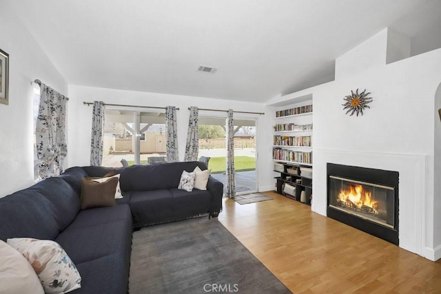 living room with a glass covered fireplace, lofted ceiling, and wood finished floors