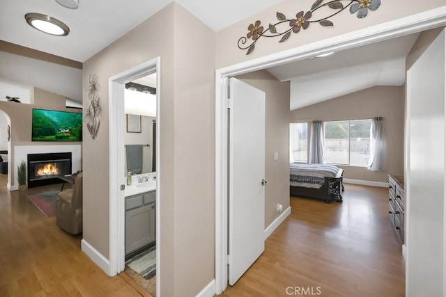 hallway with baseboards, light wood-type flooring, and lofted ceiling