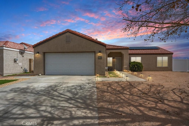 mediterranean / spanish-style home featuring stucco siding, driveway, an attached garage, solar panels, and a tiled roof