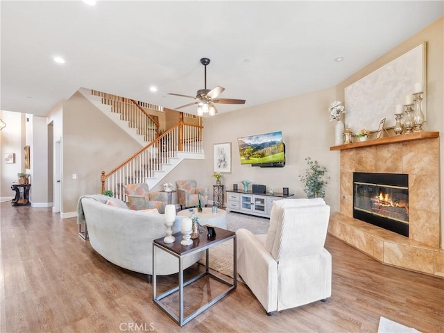 living room featuring stairway, a fireplace, a ceiling fan, and wood finished floors