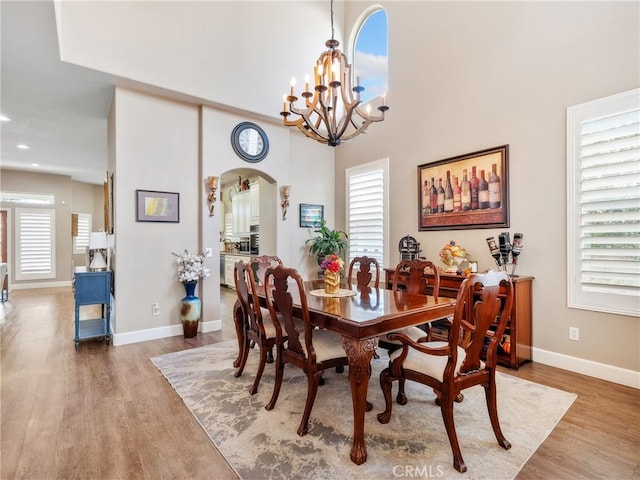 dining area with baseboards, wood finished floors, arched walkways, and a chandelier