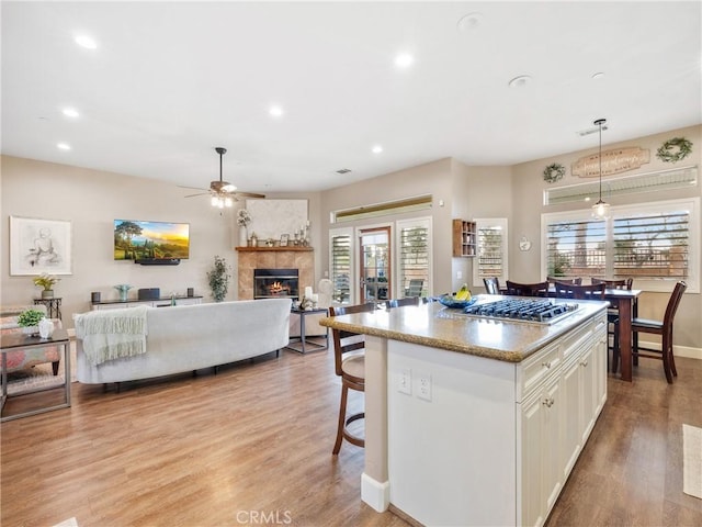 kitchen featuring light wood-style flooring, a ceiling fan, a tiled fireplace, a center island, and white cabinets