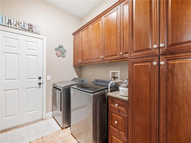 clothes washing area featuring washing machine and dryer, light tile patterned flooring, cabinet space, and baseboards