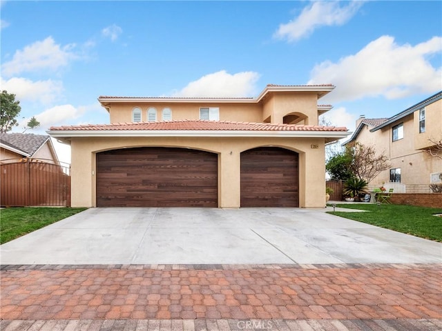 mediterranean / spanish house featuring a tiled roof, stucco siding, a garage, and fence