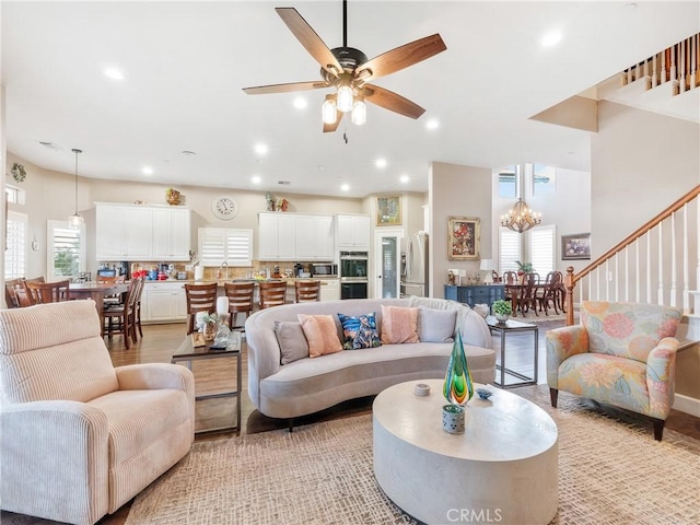 living area featuring stairway, recessed lighting, ceiling fan with notable chandelier, and a wealth of natural light