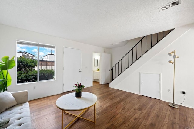 living area featuring visible vents, stairway, a textured ceiling, and wood finished floors