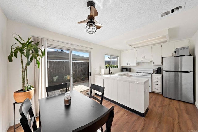 kitchen with visible vents, white gas stove, freestanding refrigerator, dark wood-type flooring, and under cabinet range hood