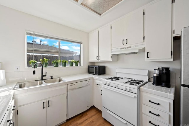 kitchen with under cabinet range hood, a sink, white cabinetry, tile countertops, and white appliances