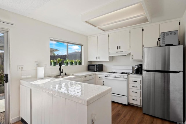 kitchen featuring white appliances, tile countertops, a peninsula, a sink, and under cabinet range hood