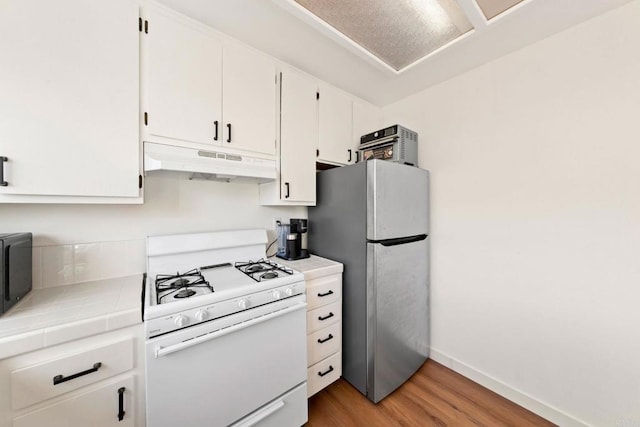 kitchen with under cabinet range hood, tile countertops, white range with gas cooktop, freestanding refrigerator, and white cabinetry