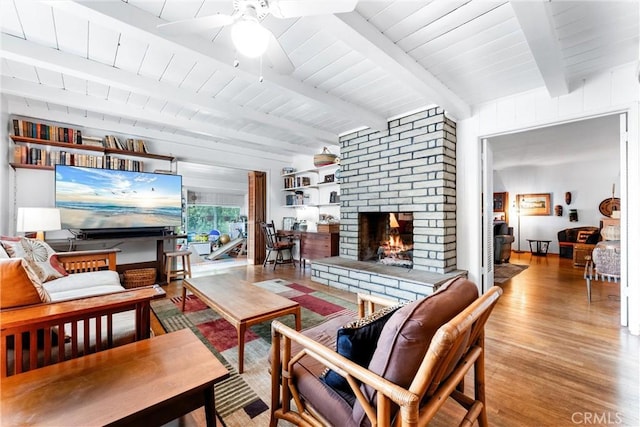 living room featuring beamed ceiling, wood finished floors, ceiling fan, and a fireplace