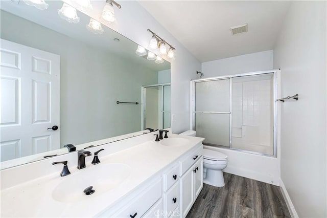 full bathroom with visible vents, toilet, a sink, wood finished floors, and double vanity