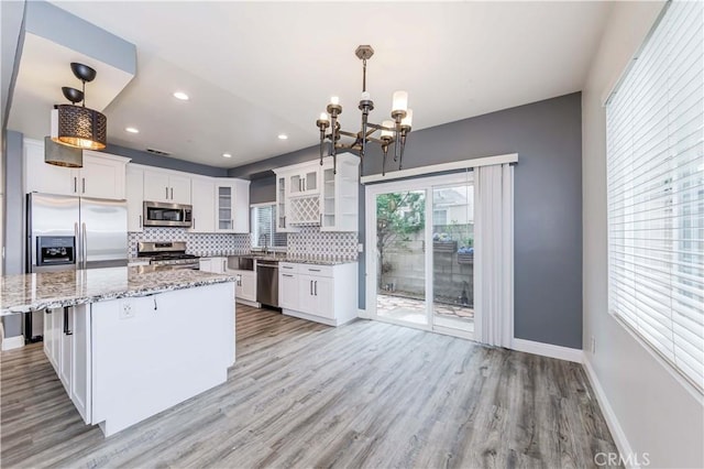 kitchen featuring decorative backsplash, white cabinets, light wood-style floors, appliances with stainless steel finishes, and a chandelier