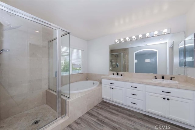 full bathroom featuring a bath, a shower stall, wood finished floors, and a sink