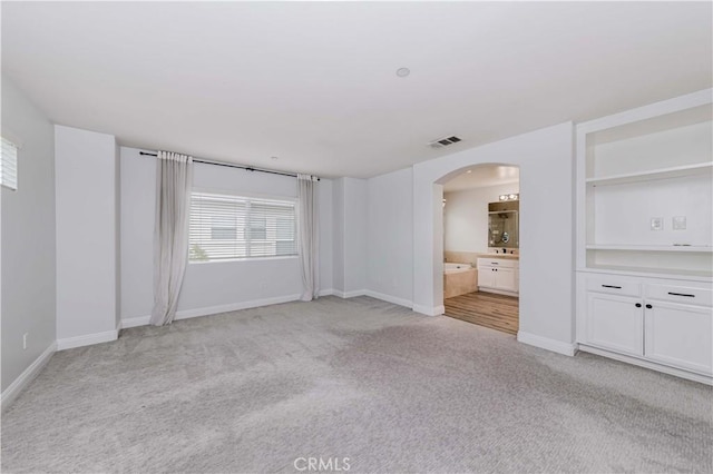 interior space with visible vents, arched walkways, light colored carpet, and baseboards