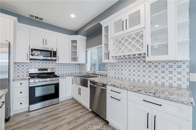 kitchen with white cabinets, light stone countertops, stainless steel appliances, and a sink