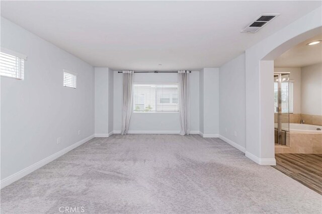 unfurnished room with arched walkways, visible vents, carpet floors, and baseboards