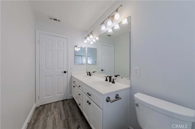 full bath with visible vents, toilet, a sink, wood finished floors, and double vanity