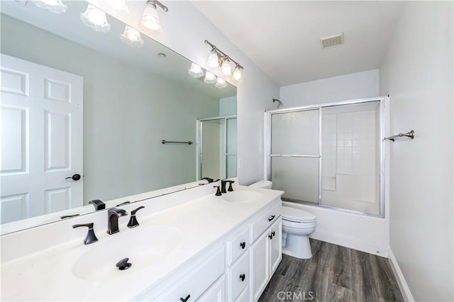 full bath featuring visible vents, toilet, a sink, wood finished floors, and double vanity