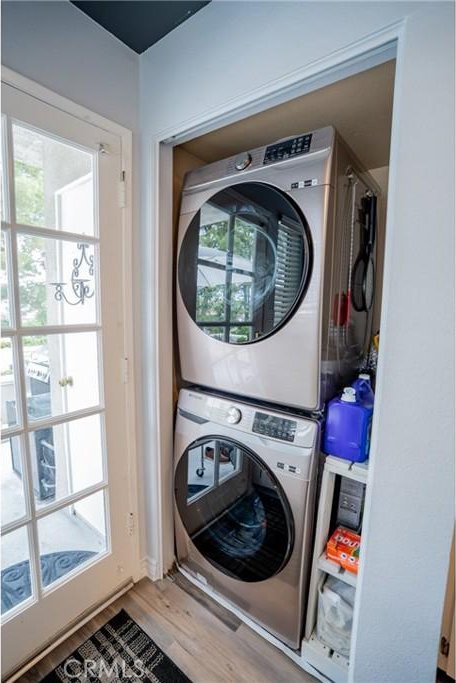 laundry room with laundry area, wood finished floors, stacked washer / drying machine, and a healthy amount of sunlight