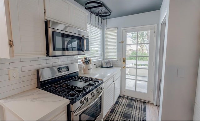 kitchen featuring backsplash, wood finished floors, stainless steel appliances, white cabinets, and light stone countertops