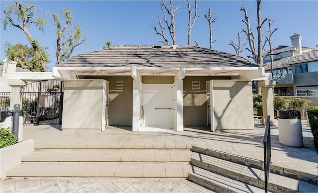 exterior space featuring stucco siding, roof with shingles, and a gate