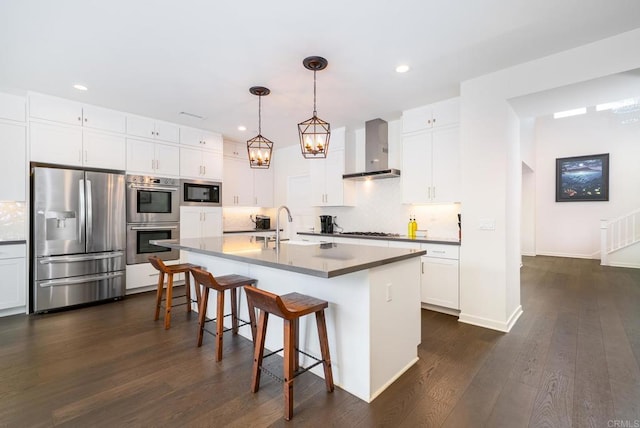 kitchen with dark wood-type flooring, wall chimney range hood, decorative backsplash, appliances with stainless steel finishes, and a sink