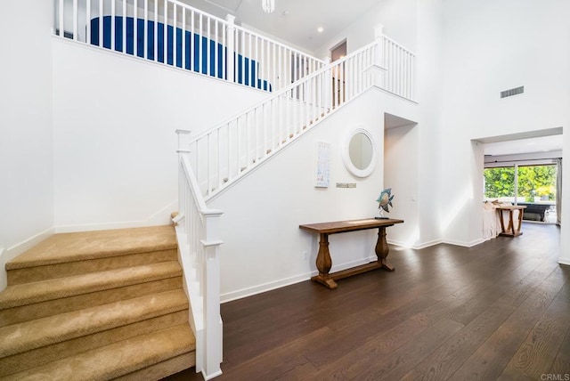 stairway with visible vents, a high ceiling, baseboards, and wood-type flooring