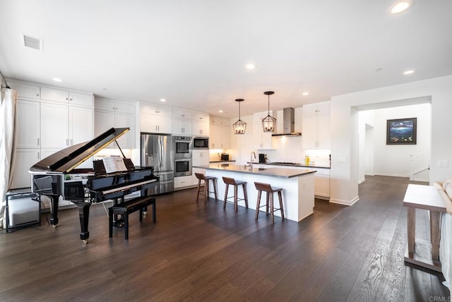 kitchen featuring visible vents, wall chimney range hood, a breakfast bar area, appliances with stainless steel finishes, and dark wood-style floors