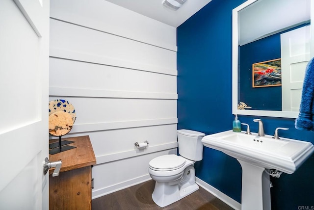 half bathroom featuring visible vents, baseboards, toilet, wood finished floors, and a sink