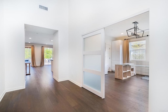 corridor featuring dark wood finished floors, a notable chandelier, baseboards, and visible vents