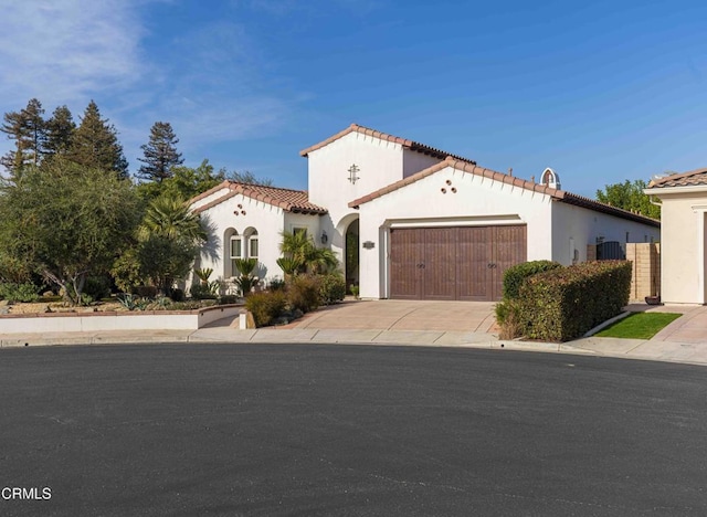 mediterranean / spanish house featuring stucco siding, driveway, an attached garage, and a tiled roof