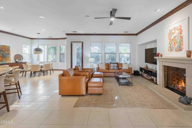 living room with a ceiling fan, light tile patterned flooring, recessed lighting, a lit fireplace, and crown molding