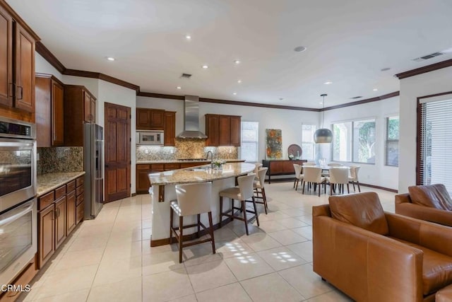 kitchen with a breakfast bar, light tile patterned flooring, appliances with stainless steel finishes, wall chimney exhaust hood, and open floor plan