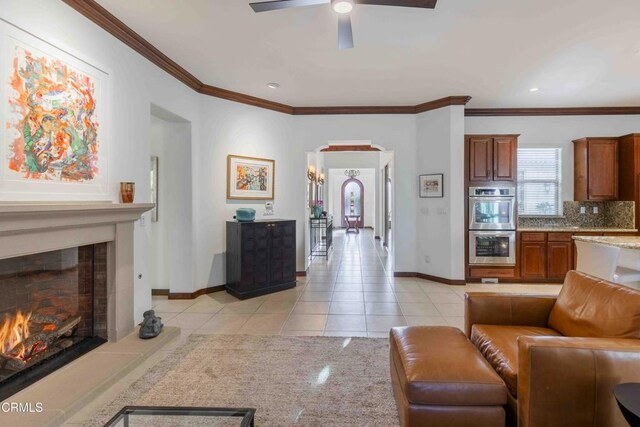 living area featuring arched walkways, light tile patterned floors, a tile fireplace, and crown molding