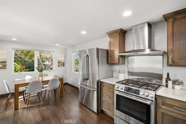 kitchen with recessed lighting, appliances with stainless steel finishes, wall chimney exhaust hood, light countertops, and dark wood-style flooring