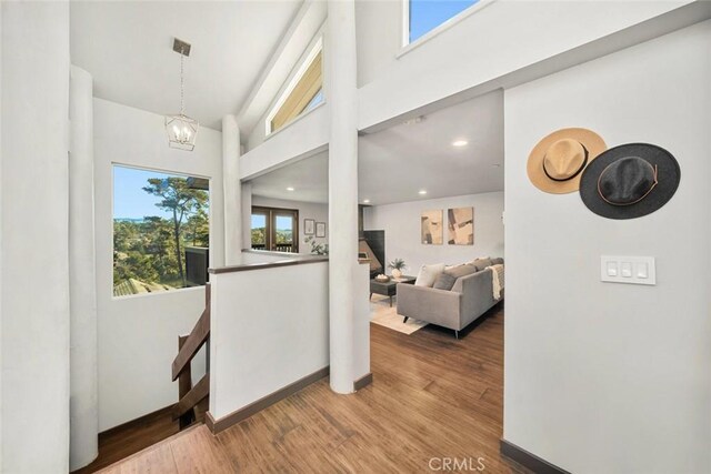 hallway with an inviting chandelier, wood finished floors, baseboards, and a towering ceiling